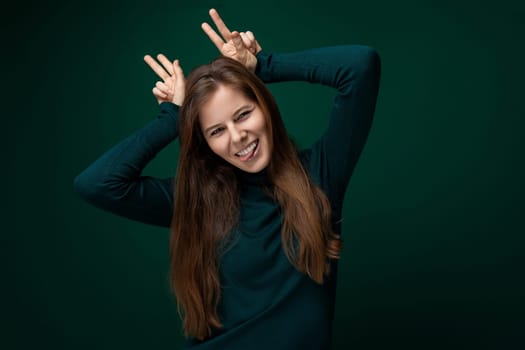 Portrait of a funny young woman with brown eyes dressed in a green turtleneck with a grimace.