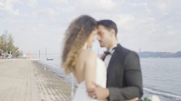 Beautiful couple in love hugs on embankment. Action. Elegant couple in suits during date on embankment. Beautiful couple of lovers tenderly embrace on embankment on sunny day.