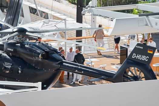 Monaco, Monte Carlo, 27 September 2022 - Rich clients visitors examine a helicopter standing on the deck of a yacht club, the largest fair yacht show, port Hercules, yacht brokers, sunny weather. High quality photo