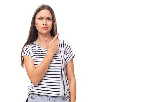 young positive pretty european brunette woman in a striped t-shirt points her finger on a white background with copy space.