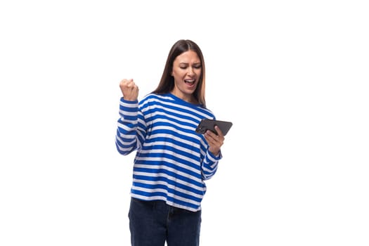 young joyful caucasian woman with dark hair dressed in a blue striped sweatshirt watches video on the phone on a white background.