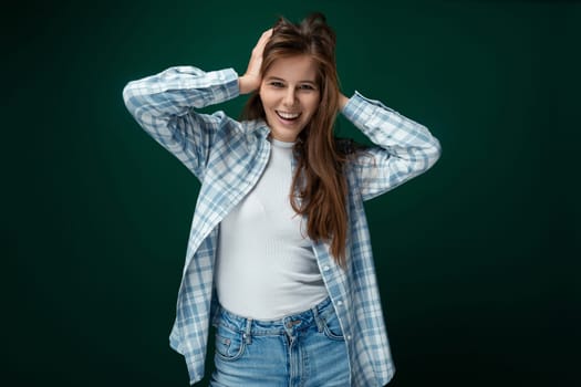Positive European woman dressed in a stylish shirt and jeans on a green studio background.