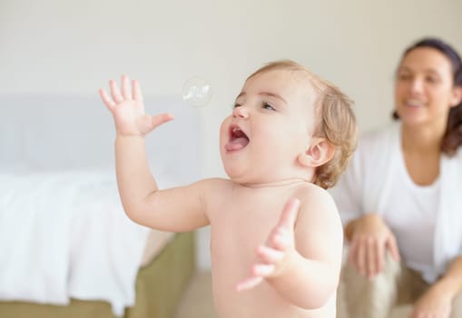 Bedroom, bubble and a baby playing with his mother in their home together for love or family bonding. Kids, smile or freedom and a young infant child having fun with a parent in an apartment.