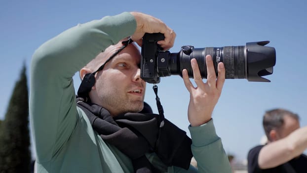 Side view of a male photographer with a professional camera outdoors. Action. Man holding camera and taking pictures