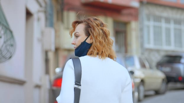 Rear view of masked woman walking. Action. Beautiful masked woman walks in slow motion. Cinematic shooting of masked woman walking down street in summer.