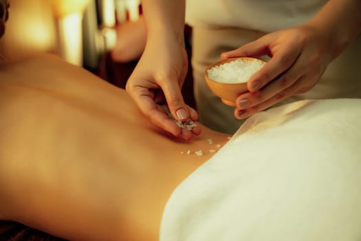 Woman customer having exfoliation treatment in luxury spa salon with warmth candle light ambient. Salt scrub beauty treatment in Health spa body scrub. Quiescent