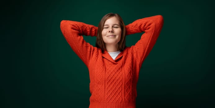 Charming young woman with brown straight hair dressed in a red sweater on a green background with copy space.