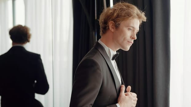 A man with a sympathetic appearance . Action . A man in an elegant suit stands next to the mirror and poses