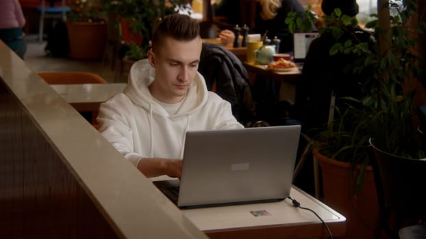 Working environment. Stock footage. A young man sitting in a cafe and working at a laptop while talking on the phone. High quality 4k footage