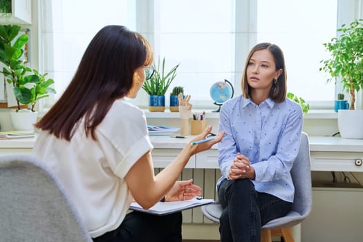 Young woman at a mental therapy session talking to female psychologist in therapist's office. Serious female patient, help support professional counselor, psychotherapist, mental health youth concept