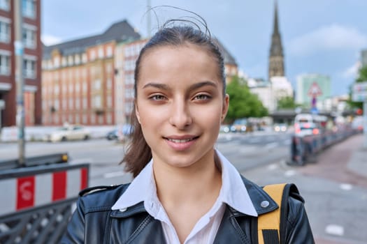 Portrait of teenage high school student, smiling confident girl 16, 17 years old with backpack looking at camera outdoor, on street of modern city. Urban life, adolescence, education, youth concept