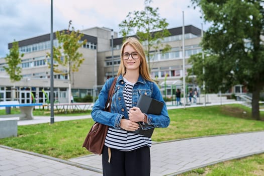 Girl student teenager outdoor near school building. Smiling teenage female with backpack digital tablet posing looking at camera. Adolescence, education, learning concept