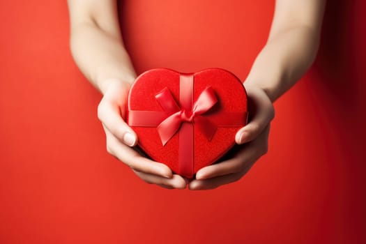 Woman's hands with a heart-shaped gift box against a red backdrop, ideal for an advertising poster, banner, or heartfelt greeting card