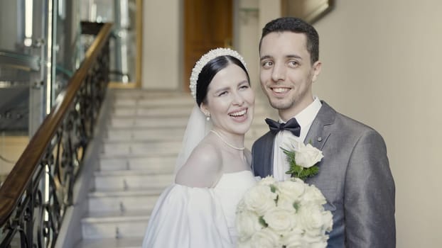 A girl in a beautiful snow- white dress with a bouquet in her hands and a grrom in official suit. Action. A wonderful touching moment of wedding