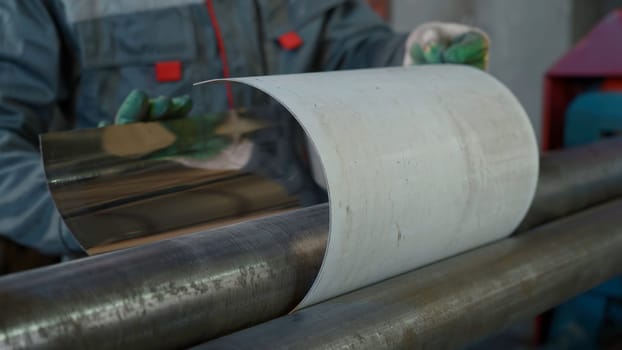 Automated machine shapes the metal sheet at the industrial plant. Creative. Machine is bending the long sheet of metal at the production facility, worker holds metal sheet under bending machine