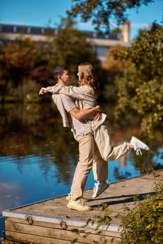 A guy carrying a girl on his back, at the beach, outdoors. River. Young Love. Handsome young man kissing his girlfriend near the river.