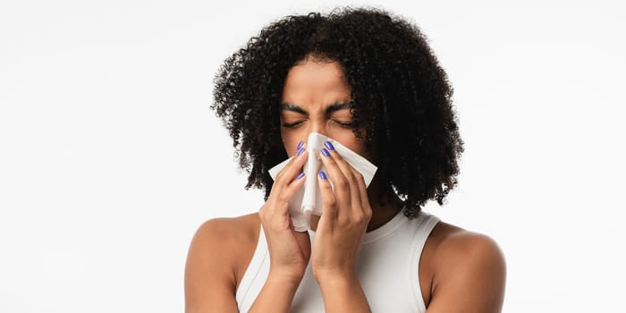 Sick young african woman blowing nose on tissue. High quality photo