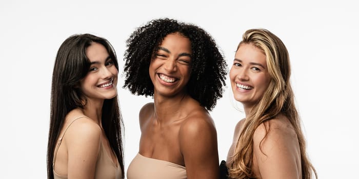 Female models of different ages celebrating their natural bodies in a studio. Three confident and happy women smiling cheerfully. Women standing together against a studio background.