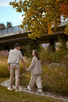 Young couple in love walking in the autumn park holding hands looking in the sunset. Closeup of loving couple holding hands while walking at sunset. The hands of the male and female lovers who hold hands walk forward high with blurred background