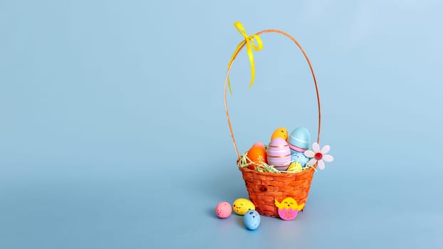 Easter wicker basket filled with decorative multi colored eggs on a light blue background.