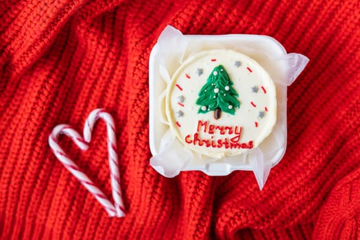 Christmas cupcake with a candy cane heart on a red knitted background. Merry christmas cake inscription