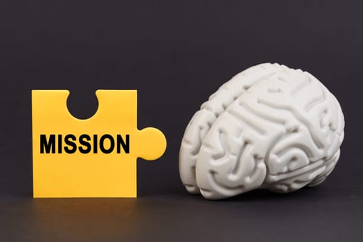 On a black surface there is a brain and a yellow puzzle with the inscription - Mission. Education and business concept.