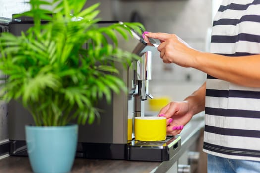 A young woman makes fresh flavored coffee with a modern coffee machine in her kitchen.