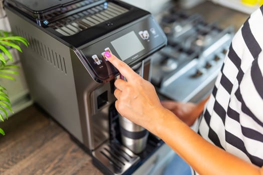 A young woman makes fresh flavored coffee with a modern coffee machine in her kitchen.