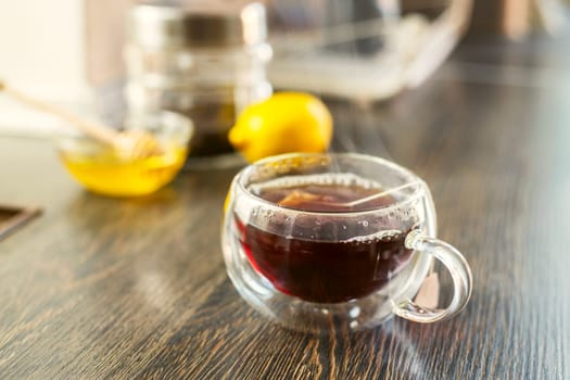 Cup of hot black tea, bowl with honey and lemon on a wooden table.