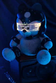 toy bear dressed in leather BDSM belts, headphones and glowing glasses in neon light listens to music. dark background