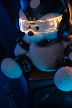 toy bear dressed in leather BDSM belts, headphones and glowing glasses in neon light listens to music. dark background