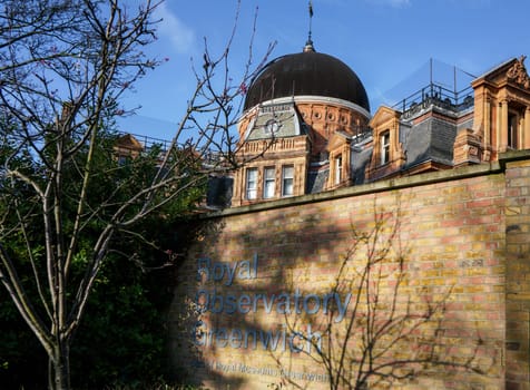 London, United Kingdom - February 02, 2019: Royal Observatory Greenwich building dome (founded 1675) with sign near entrance on sunny spring day.