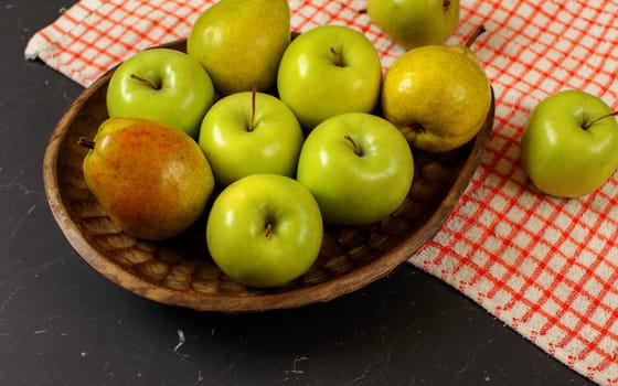 Wooden carved bowl with apples and pears, red chequered tablecloth on black marble like board