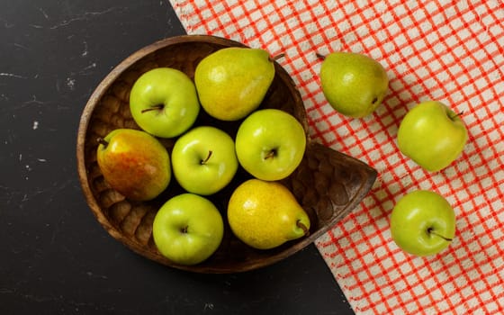 Flat lay photo - vintage wood carved bowl with apples and pears, red chequered tablecloth on black board