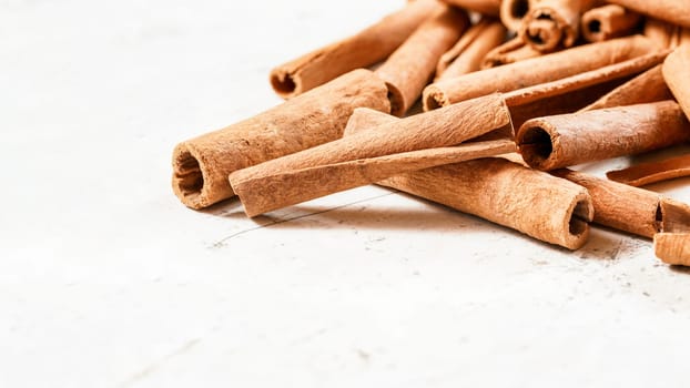 Heap of natural organic cinnamon bark sticks on white board, space for text down.