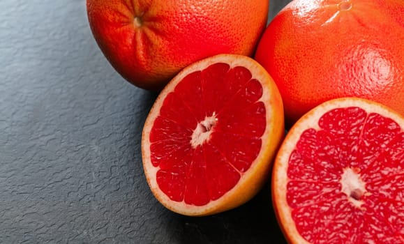 Pink grapefruits halves, whole citrus in background, on black slate like board