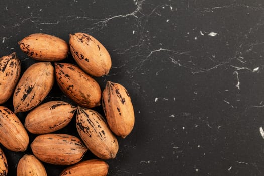 Whole pecan nuts on black marble like board, space for text right, photo from above