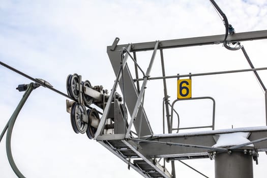 Steel ropes over wheels in mechanism on top of ski chair lift support pillar, number 6 on yellow plate, bright sky background