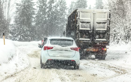 Traffic jam on forest road, cars and trucks moving slowly - mountain pass during heavy snow blizzard