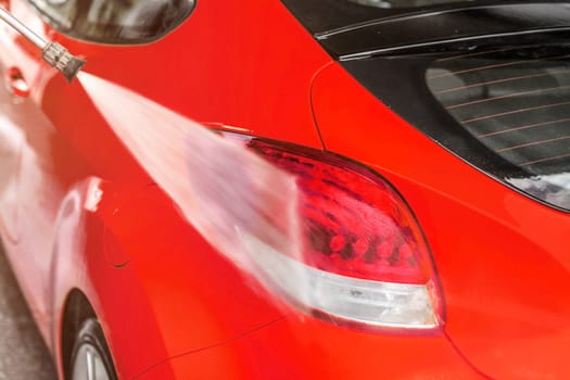 Rear light of red car washed in self service carwash, water spraying on surface