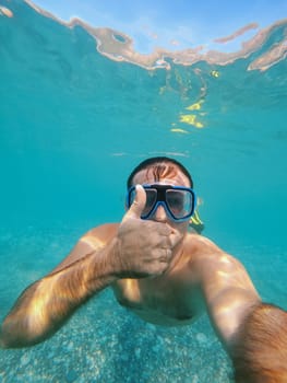 Man in goggles and fins swims under water with his thumb up. High quality photo
