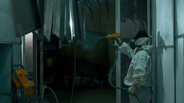 Process of powder coating of metal parts at a steel factory. Creative. Worker in protective suit with paint gun