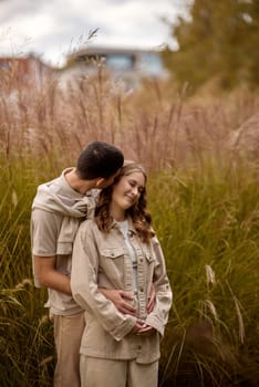 Happy couple on autumn walk outdoors. Two lovers in autumn park. Love and tender touch. Gentle hugs. Young man and woman in classic autumn colors outfit on a romantic date in a park. Young girl and guy with blond hair kisses, show love, affection. Boy and girl of European appearance with warm clothes, pictures with soft background bokeh blur fall. Concept of happiness,