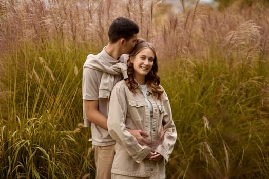 Happy couple on autumn walk outdoors. Two lovers in autumn park. Love and tender touch. Gentle hugs. Young man and woman in classic autumn colors outfit on a romantic date in a park. Young girl and guy with blond hair kisses, show love, affection. Boy and girl of European appearance with warm clothes, pictures with soft background bokeh blur fall. Concept of happiness,