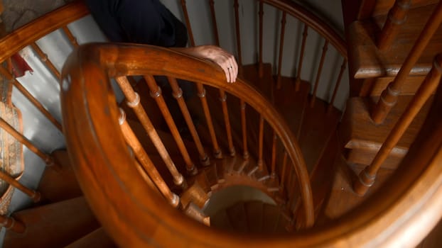 A twisted staircase made of wood. Action. A man in black clothes going up and down a rounded staircase. High quality 4k footage