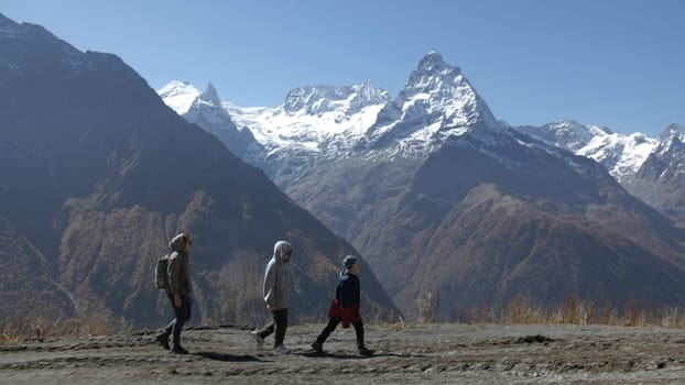 Family walks on background of mountain valley with snowy peaks. Creative. Women with child are walking in mountain valley on sunny day. Family hiking with child in valley with rocky mountains.