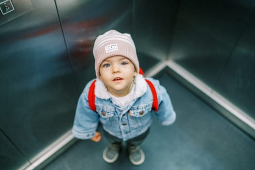Little girl stands in an elevator with her head up. High quality photo