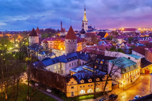 Aerial view of Tallinn Medieval Old Town with St. Olaf's Church and Tallinn City Wall illuminated in evening with dramatic cloudscape, Estonia