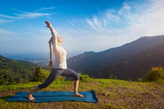 Yoga outdoors - woman doing yoga asana Virabhadrasana 1 - Warrior pose posture outdoors in Himalayas mountains in the morning