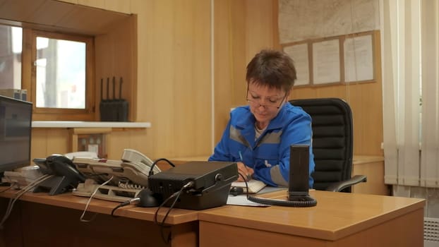 Woman in blue uniform working at the table. Clip. Emergency worker doing administrative work and writing